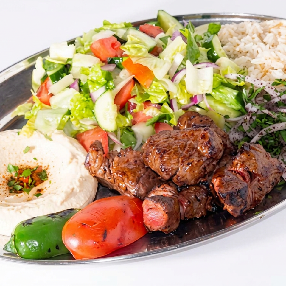 Mediterranean platter featuring grilled meat, rice, salad, hummus, grilled tomatoes and peppers, and sliced onions.