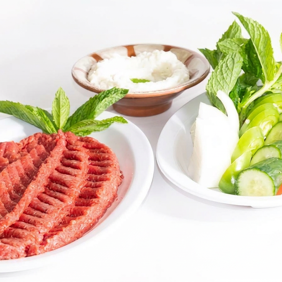 Grilled minced meat patties garnished with mint, served with sliced cucumber, tomato, onion, and a bowl of yogurt sauce.